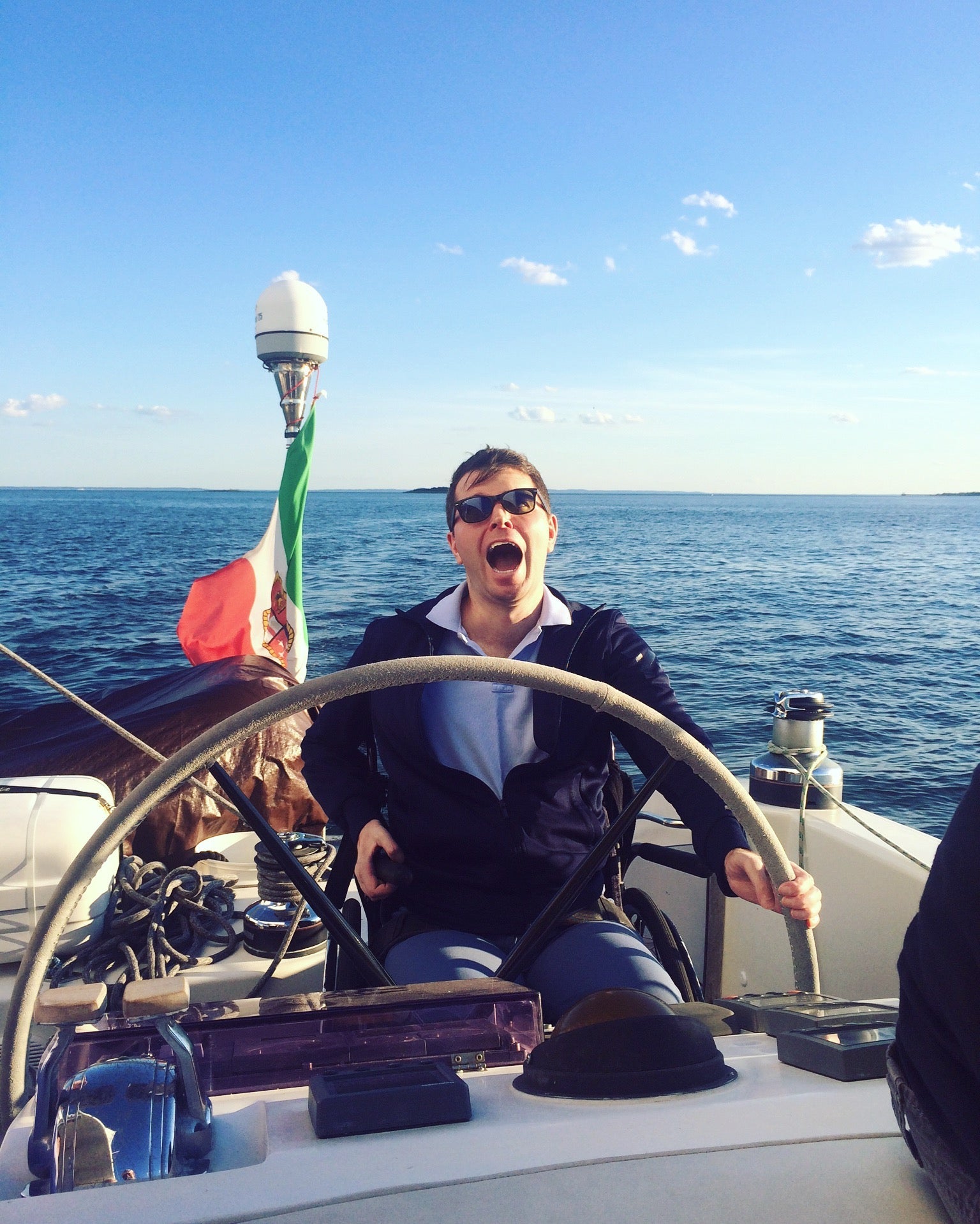 Francesco Clark laughing at the wheel of a catamaran, seated in his wheelchair, open water behind him.